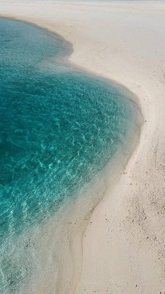 Aerial view of turquoise shallows meeting white sand on an Aruban beach
